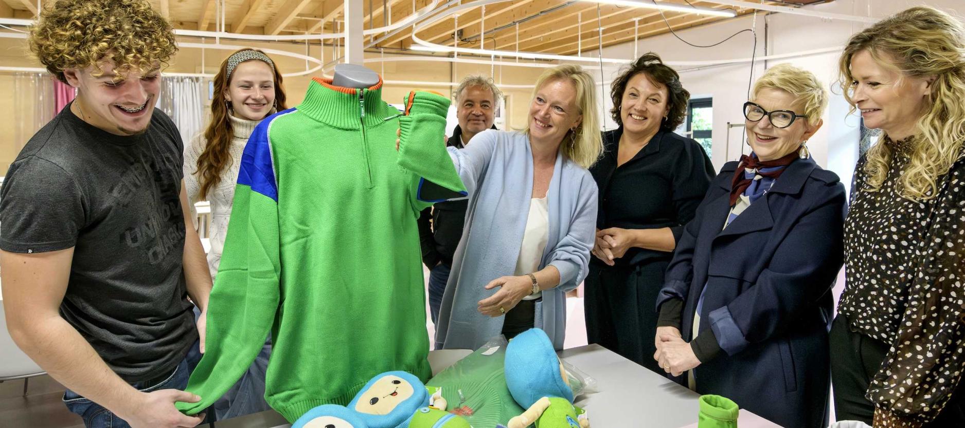 wethouder Chantal Zeegers (Klimaat, Bouwen en Wonen) poseert samen met 6 medewerkers / studenten van het Zadine. Ze bewonderen de trui en poppen die gemaakt zijn door de studenten.