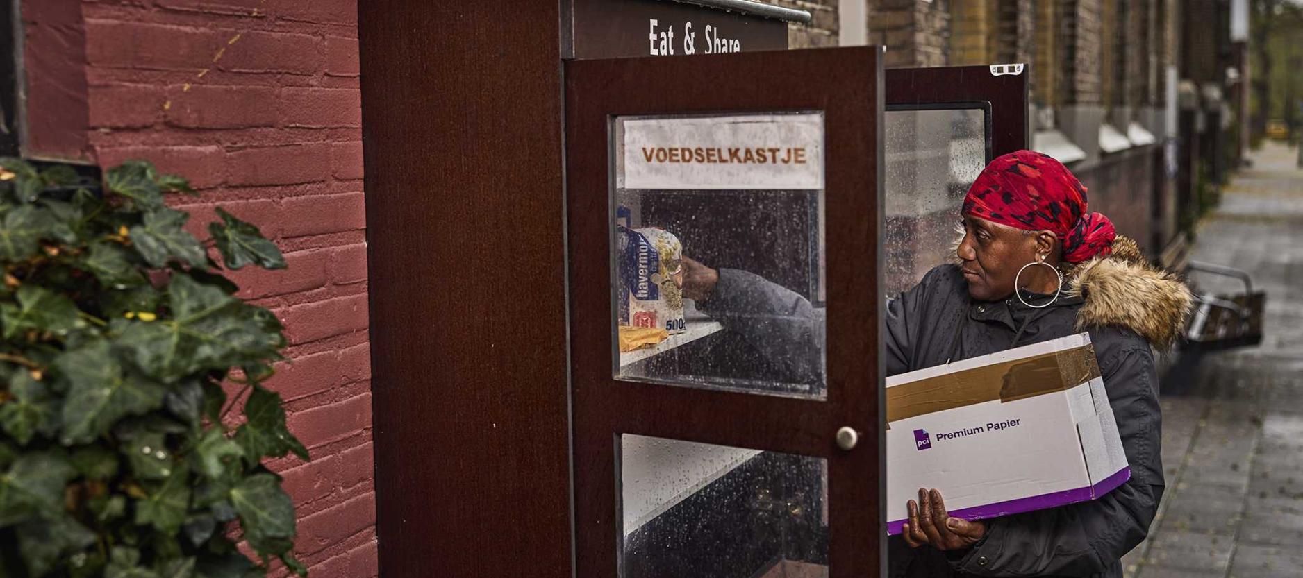 vrouw stop pak havermout in een houten voedselkastje dat aan de gevel in een straat hangt.