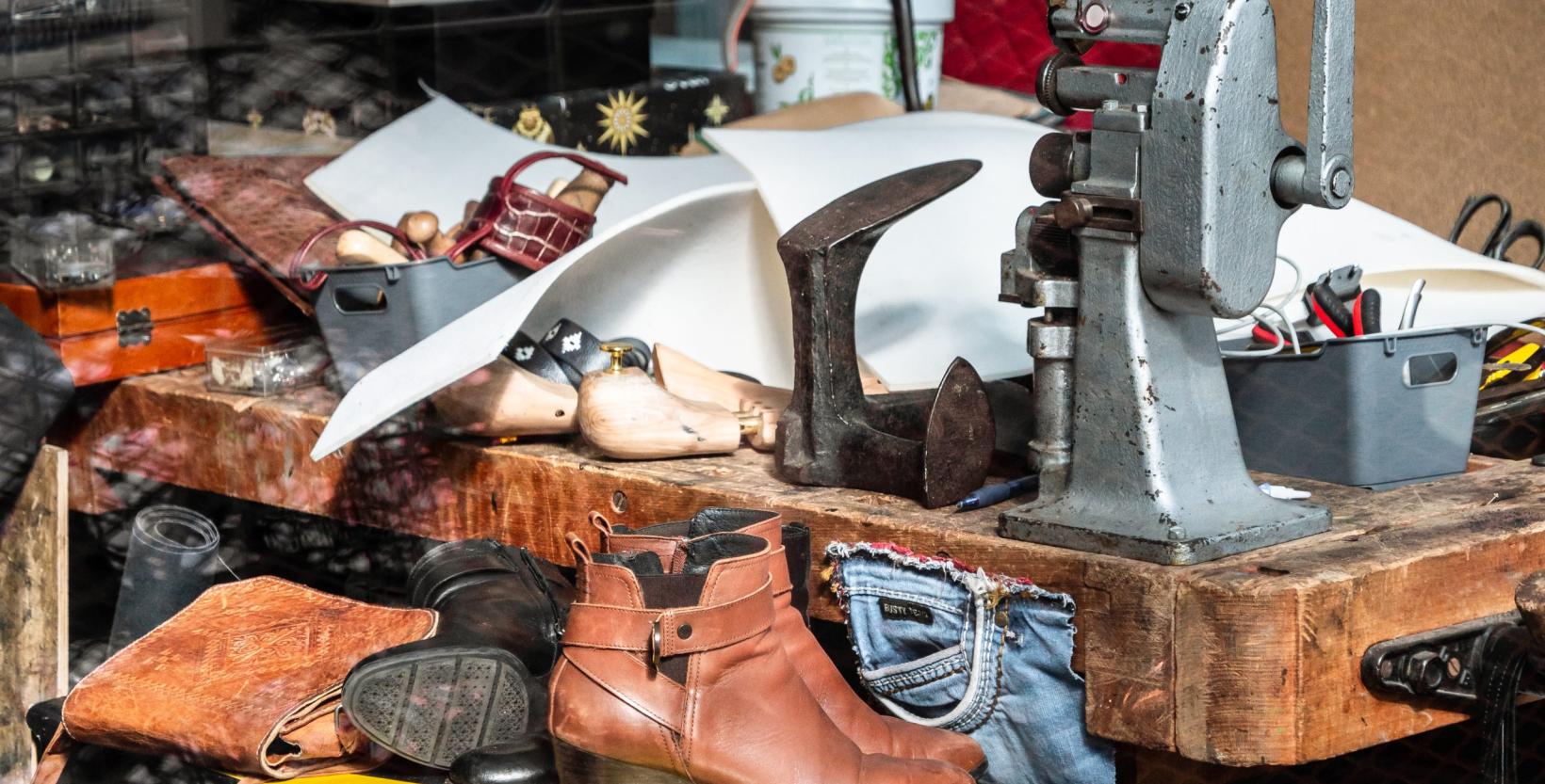 clos-up van de werkbank uit het atelier. houten werkbank, met ijzeren leest en andere metalen gereedschap, er staan verschillende schoenen op de voorgrond.