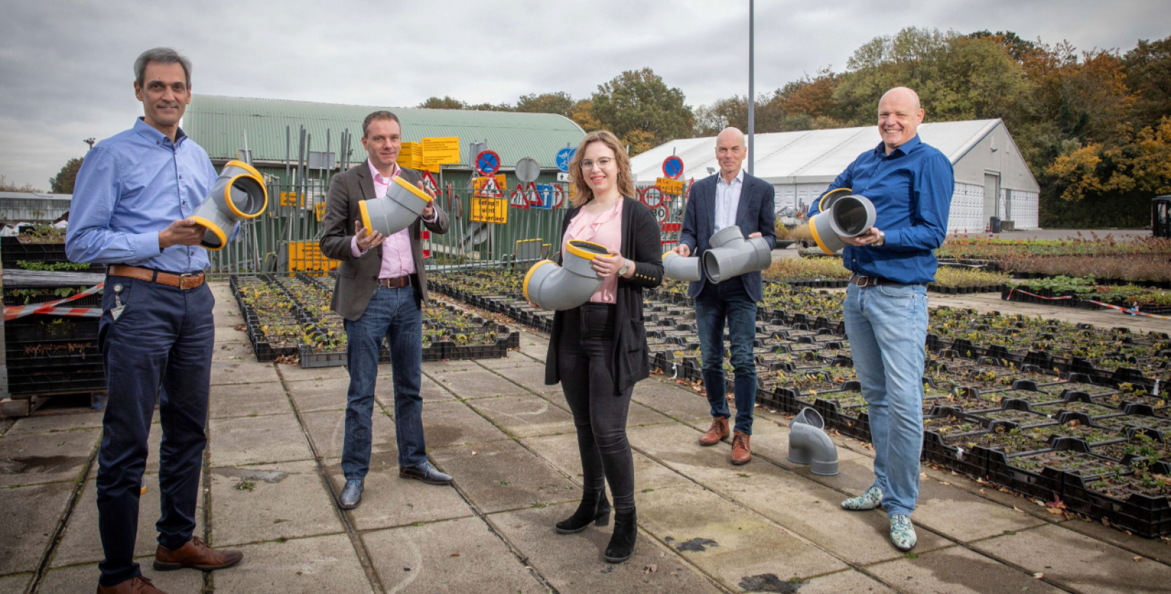 Op de foto vijf personen. Allemaal hebben ze een onderdeel van kunststof rioolbuizen beet.