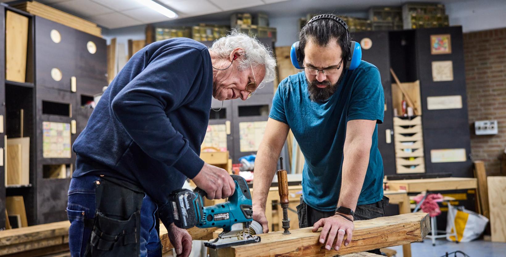 Twee personen zijn in een werkplaats aan het klussen met hout.